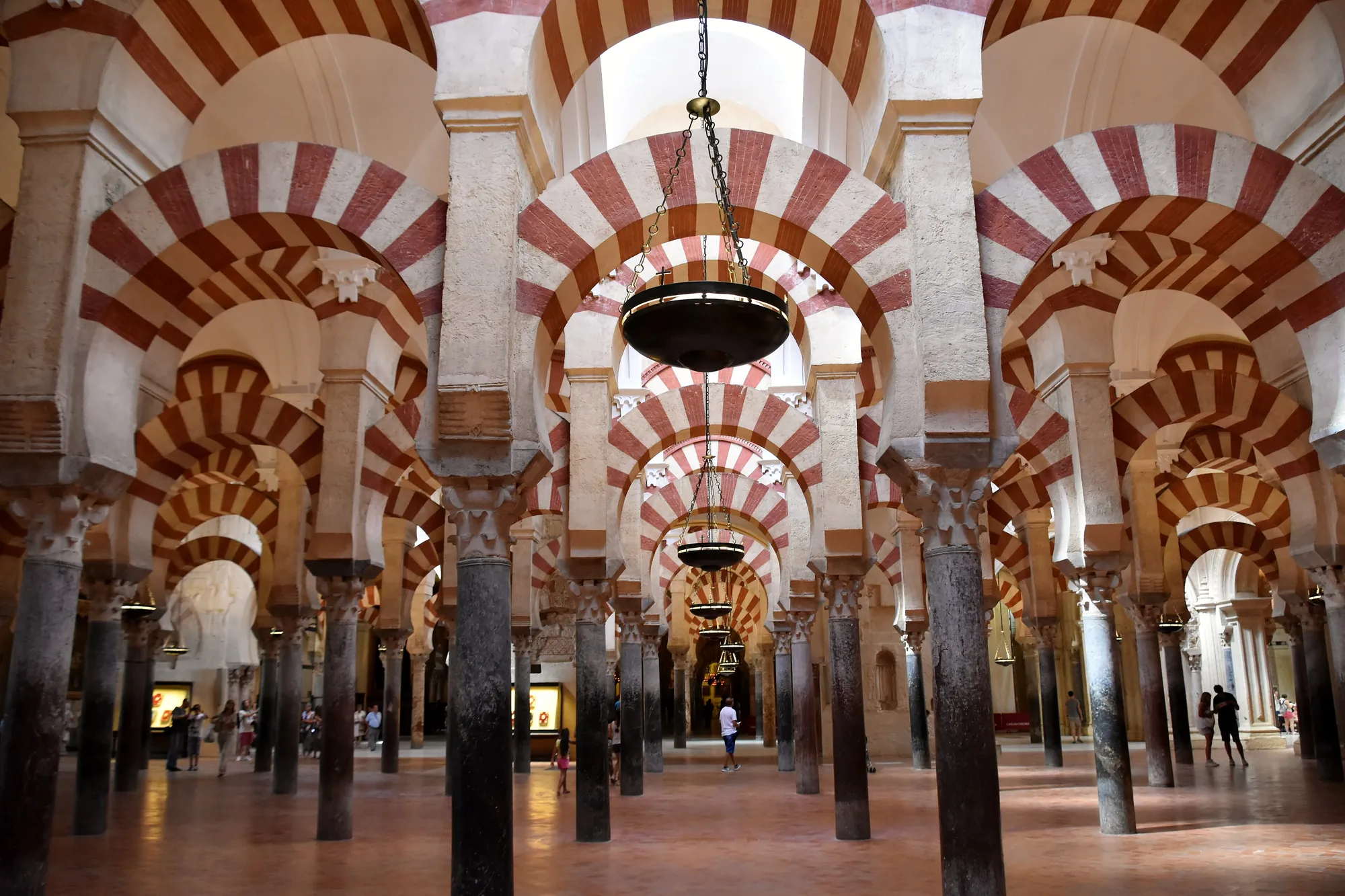 The forest of red-and-white striped arches inside the Great Mosque of Córdoba, with a hanging lamp and visitors far down the aisle